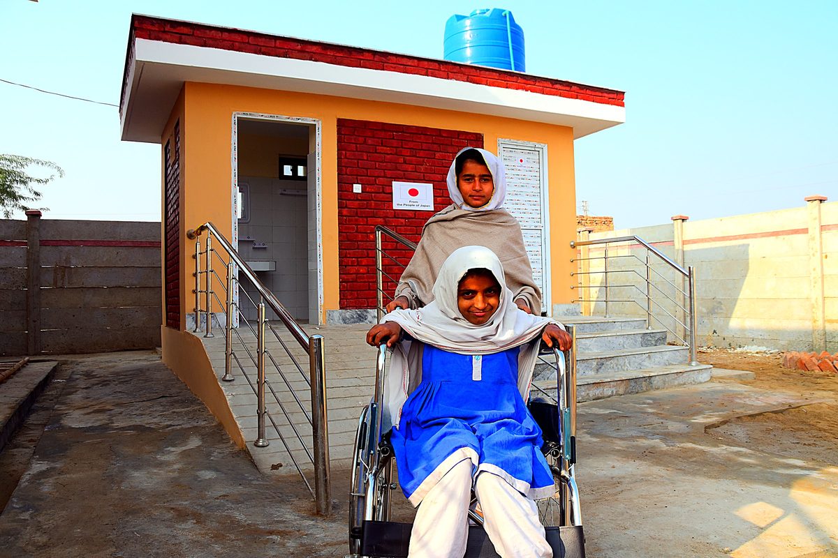 A wheelchair-accessible school toilet block with ramps, handrails and a rooftop water tank.